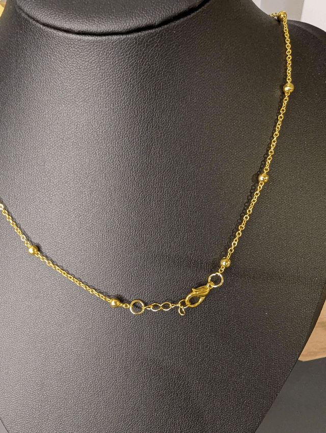 Collier long, sautoir, avec une chaine de couleur or et un pendentif en cuir et en tissus enduit en forme de rond et de cœur.
