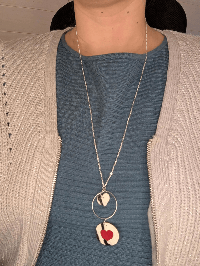 Collier long, sautoir, avec une chaine de couleur argent, un pendentif en cuir et en tissus enduit en forme de rond et de cœur