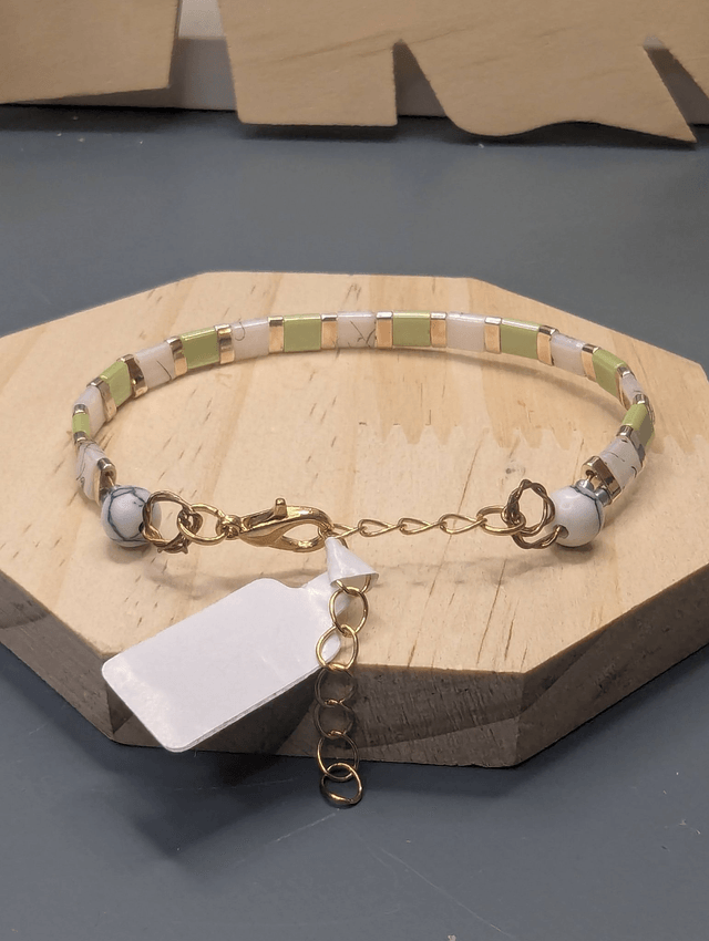 Bracelet avec des perles plate en verre blanches et vertes et des perles en métal doré. Le fermoir et la chaine fermoir sont de couleur or.
