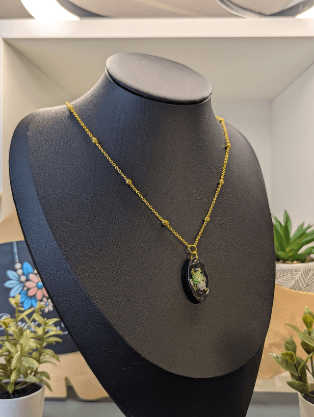 Collier mi long avec une chaine de couleur argent et un pendentif en résine noire avec des fleurs séchés. 