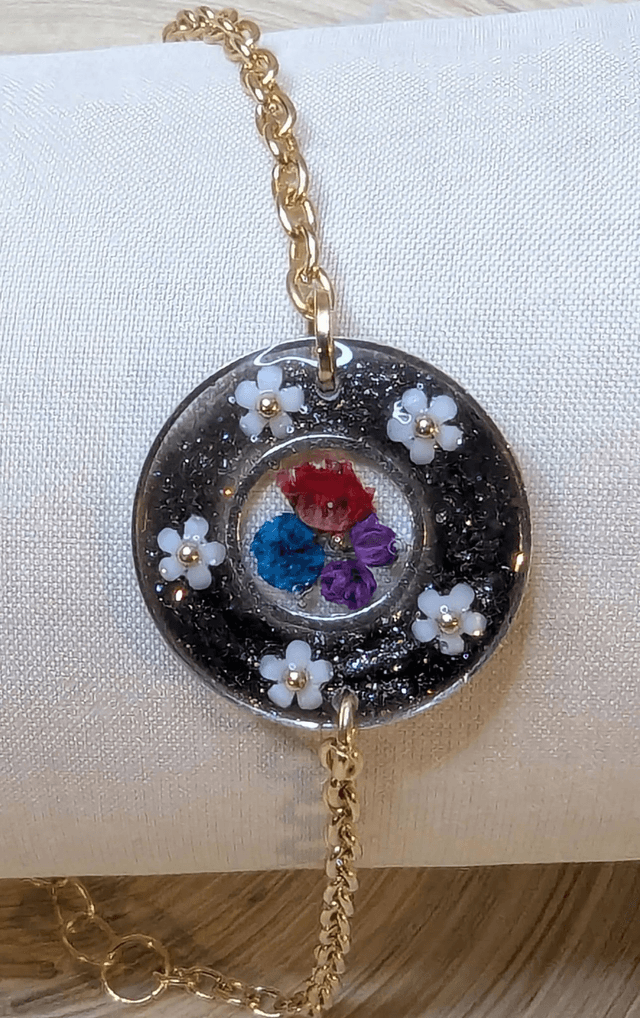 Bracelet avec une chaine de couleur or, le pendentif est en résine noir avec des fleurs séchés, le fermoir est en or. 