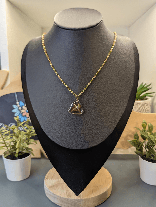 Collier avec pendentif en résine transparente te marron en forme de triangle.