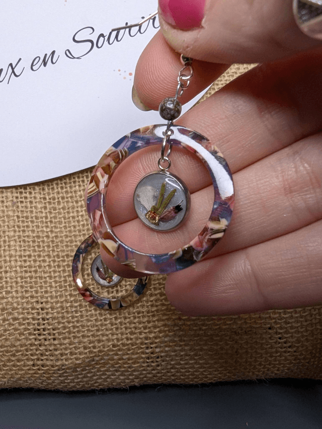 Boucles d'oreilles avec 2 pendentifs en cercle en résine coloré rose et violet, avec des fleurs, et des perle naturelle, le fermoir est en argent. 