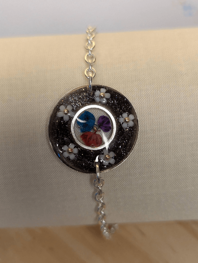 Bracelet avec une chaine de couleur argent, un pendentif en résine noir avec des fleurs séchés, le fermoir est en argent.