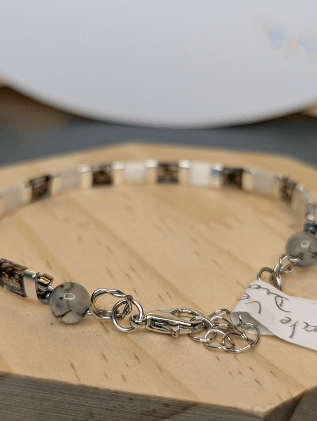 Bracelet en perles plate en verre blanc avec des  perles d'espacement en métal argenté. Le fermoir et la chaine fermoir sont en argent.