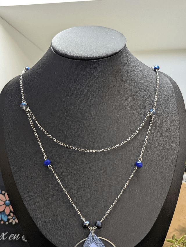 Collier long, sautoir, avec double chaine de couleur argent et un pendentif en cuir et en tissus enduit en forme de goutte et de cœur bleu.