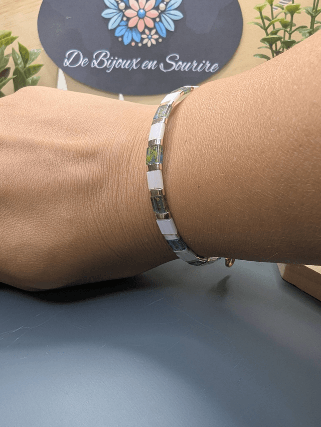 Bracelet avec des perles plate en verre blanches et bleu et des perles en métal doré. Le fermoir et la chaine fermoir sont de couleur or.