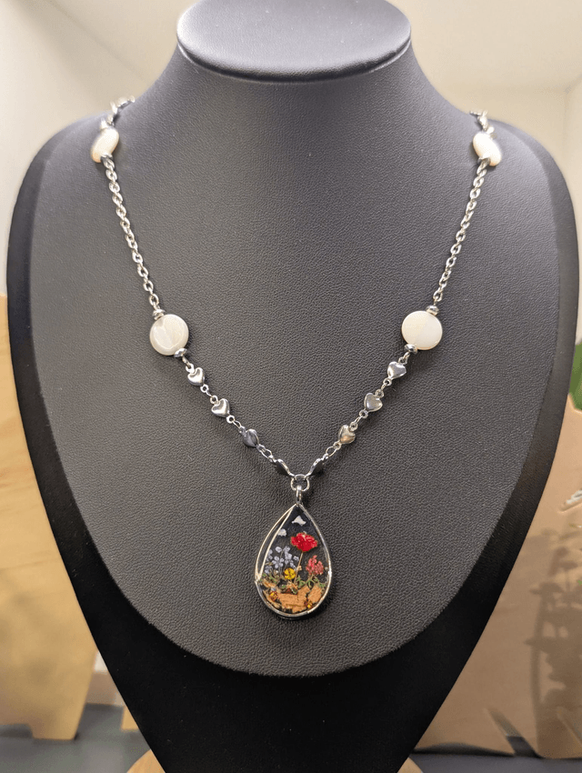 Collier mi long avec deux chaines de couleurs argent, des perles de nacre et un pendentif en résine avec fleurs séchés. 