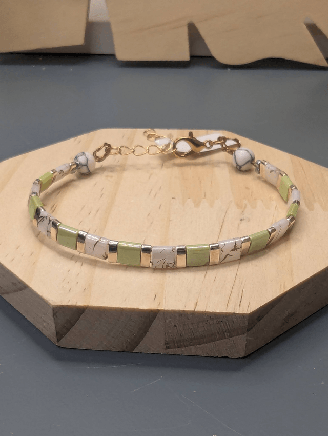 Bracelet avec des perles plate en verre blanches et vertes et des perles en métal doré. Le fermoir et la chaine fermoir sont de couleur or.