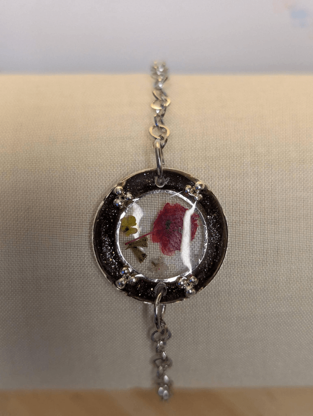 Bracelet avec une chaine en argent, un pendentif en résine noir, avec des fleurs séchés rouge, le fermoir est en argent.