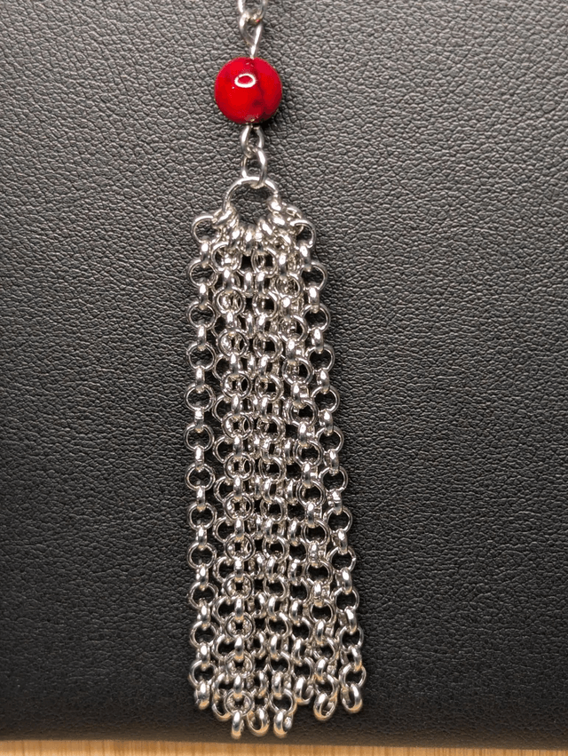 Collier long, sautoir, avec une chaine de couleur argent, des perles naturelles de turquoise rouge, et un pompon en chaine argentée. 