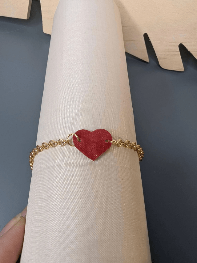 Bracelet en chaine de couleur or en forme de cœur en cuir et tissus enduit rouge, le fermoir est de couleur or. 