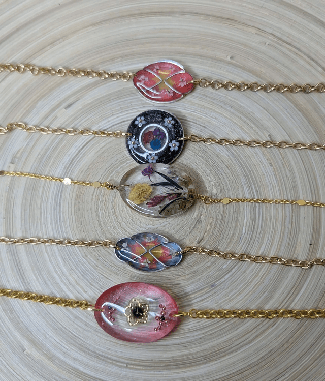 Bracelet avec une chaine de couleur or et un pendentif en résine rose transparent, motif fleur, le fermoir est en or.