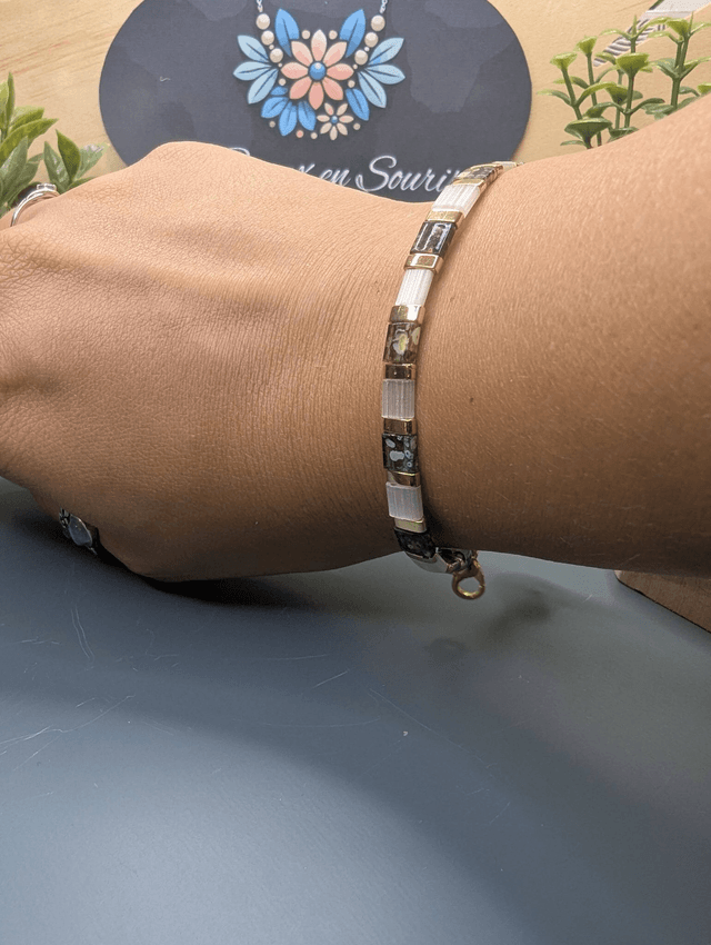 Bracelet avec des perles plate en verre blanches et verts d'eau et des perles en métal doré. Le fermoir et la chaine fermoir sont de couleur or.