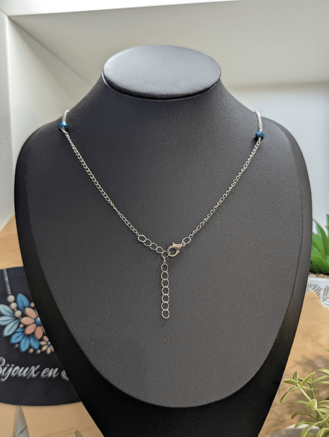 Collier long, sautoir, avec double chaine de couleur argent et un pendentif en cuir et en tissus enduit en forme de goutte et de cœur bleu.