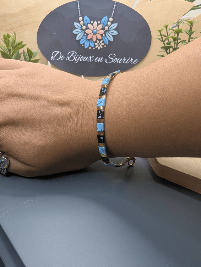 Bracelet avec des perles plate en verre noires et bleus et des perles en métal doré. Le fermoir et la chaine fermoir sont de couleur or.