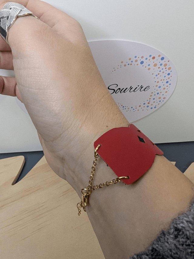 Bracelet manchette en cuir rouge, avec du tissus enduit bleu foncé (résistant), une chaine en or. Le fermoir est de couleur or.