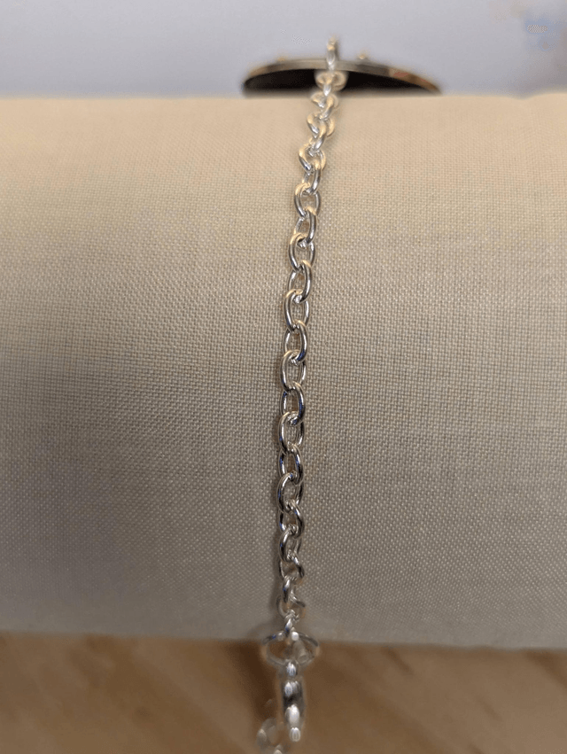  Bracelet avec une chaine de couleur argent, un pendentif en résine noir avec des fleurs séchés, le fermoir est en argent.