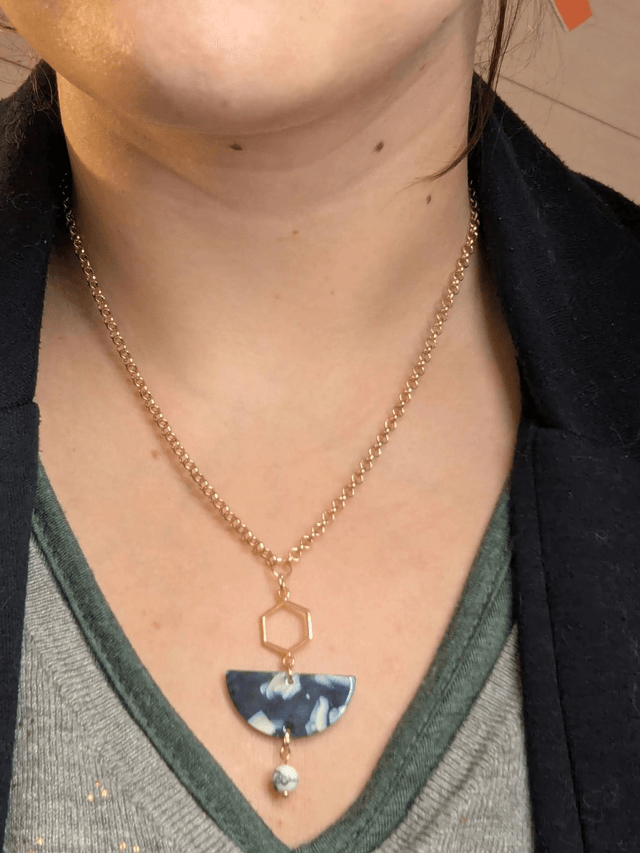 Collier mi long avec une chaine de couleur or et un pendentif en résine bleu et blanc, et un pendentif en métal doré. 