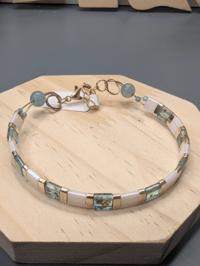 Bracelet avec des perles plate en verre blanches et bleu et des perles en métal doré. Le fermoir et la chaine fermoir sont de couleur or.