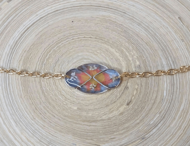 Bracelet avec une chaine de couleur or, pendentif en résine bleu, rose et jaune avec des petites fleurs blanches, le fermoir est en or.