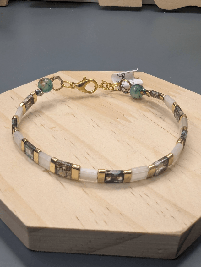 Bracelet avec des perles plate en verre blanches et verts d'eau et des perles en métal doré. Le fermoir et la chaine fermoir sont de couleur or.