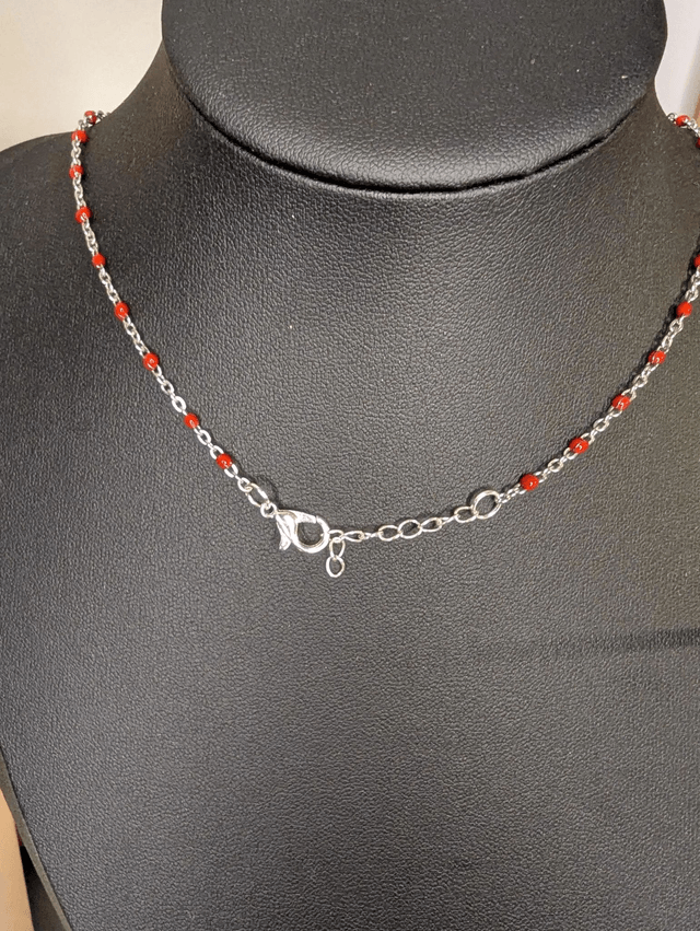 Collier mi long avec une chaine de couleur argent et rouge, avec un pendentif en cuir et en tissus enduit en forme de rond et de cœur. 