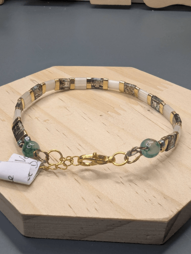 Bracelet avec des perles plate en verre blanches et verts d'eau et des perles en métal doré. Le fermoir et la chaine fermoir sont de couleur or.