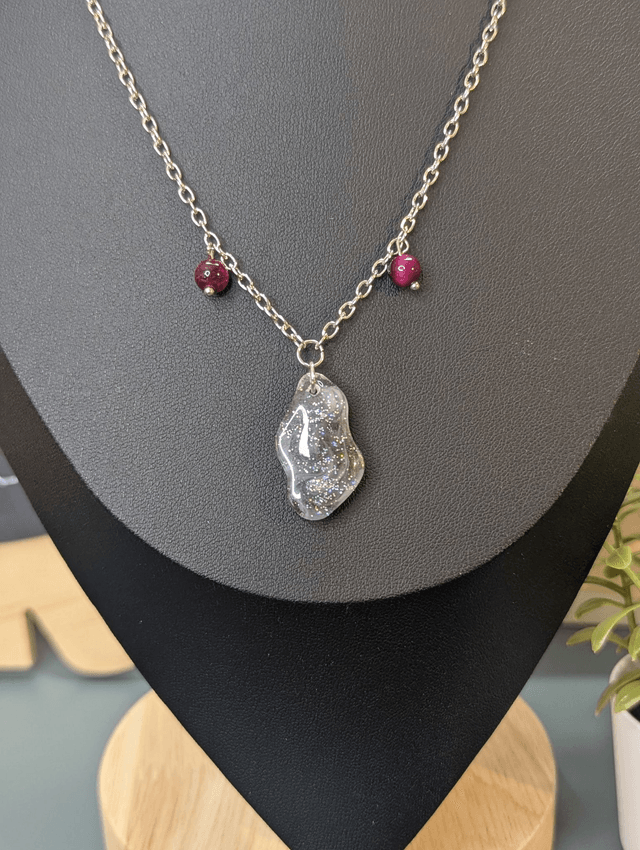 Collier mi long avec une chaine de couleur argent, un pendentif en résine noire et gris pailleté et des perles naturelles rose. 