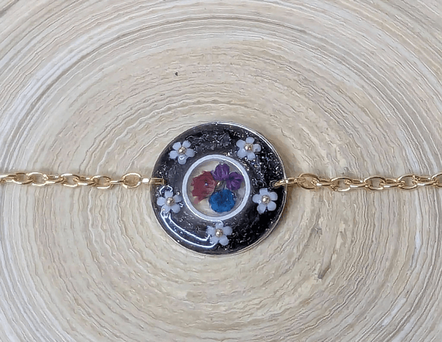 Bracelet avec une chaine de couleur or, le pendentif est en résine noir avec des fleurs séchés, le fermoir est en or. 