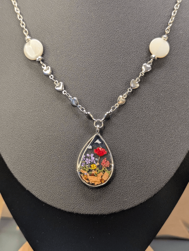 Collier mi long avec deux chaines de couleurs argent, des perles de nacre et un pendentif en résine avec fleurs séchés. 