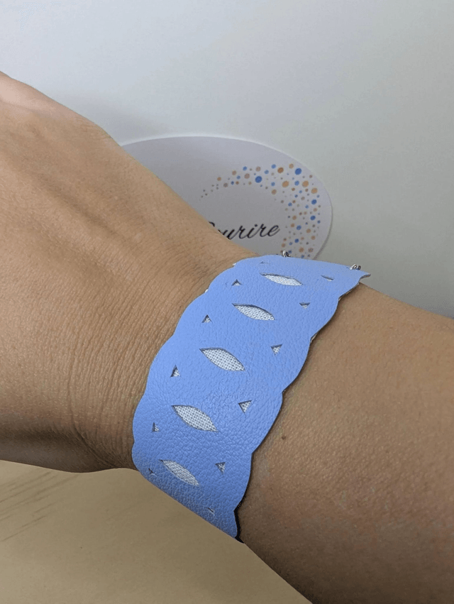 Bracelet manchette en cuir bleu lisse, avec du tissus enduit blanc (résistant), une chaine couleur argent. Le fermoir est de couleur argent.