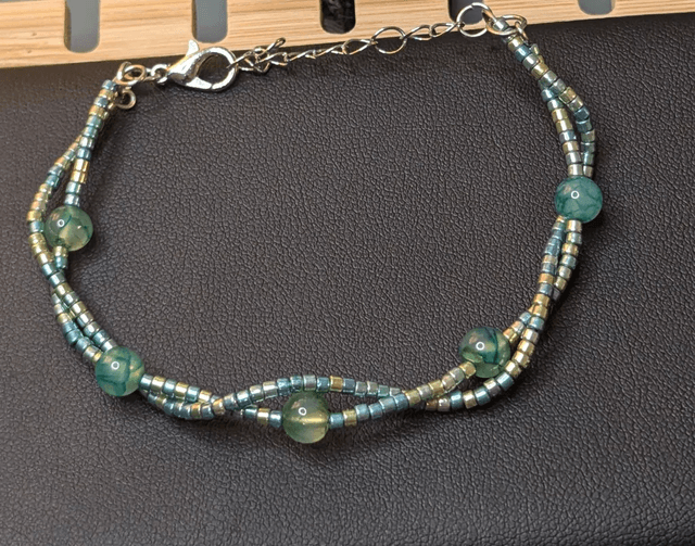 Bracelet torsadé vert avec des perles de  Miyuki en verre et des perles naturelles, montées sur fil de fer. Le fermoir est en couleur argenté.