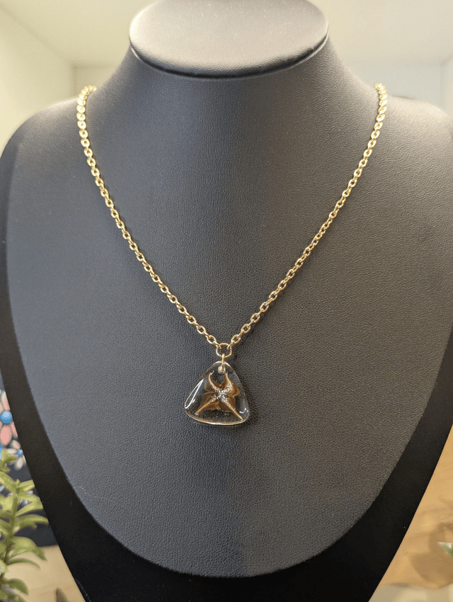 Collier avec pendentif en résine transparente te marron en forme de triangle.