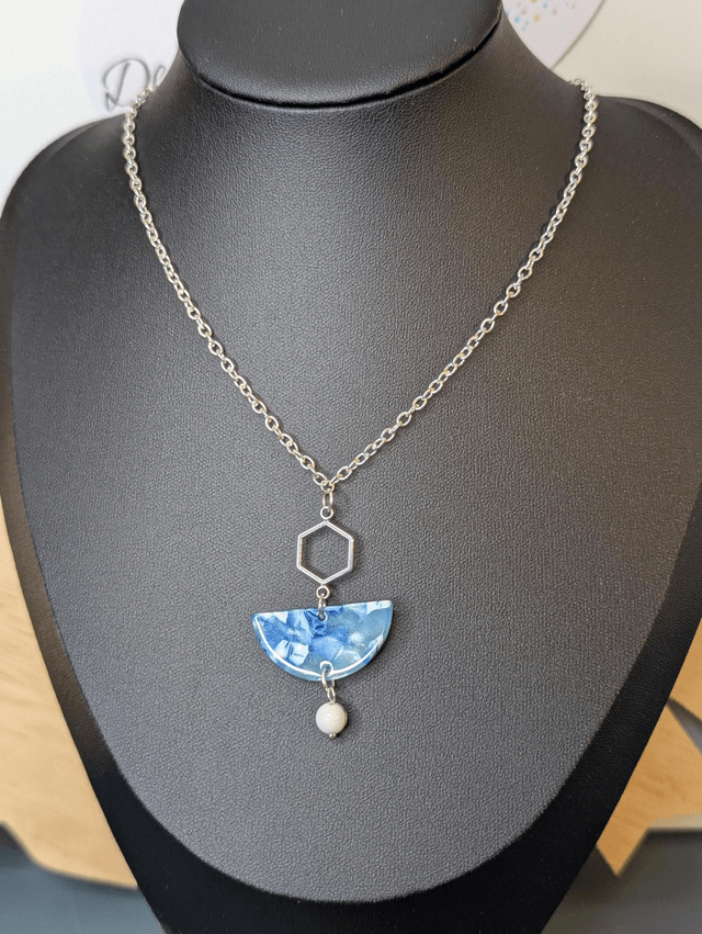 Collier mi long avec une chaine de couleur argent et un pendentif en résine bleu et blanc, et un pendentif en métal argenté. 