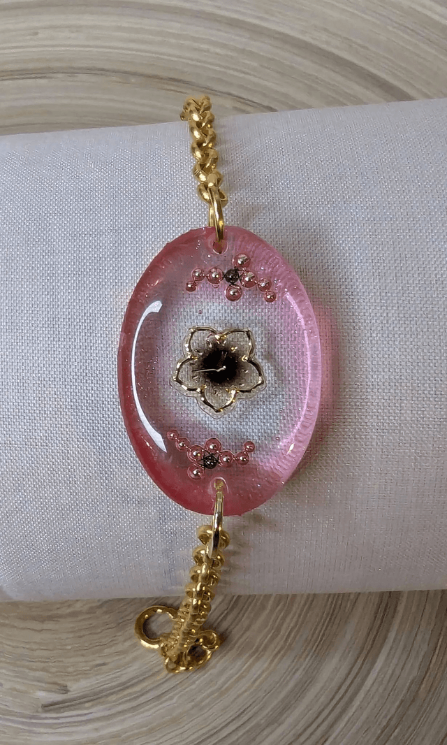 Bracelet avec une chaine de couleur or et un pendentif en résine rose transparent, motif fleur, le fermoir est en or.