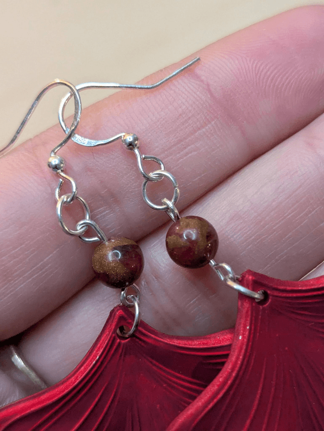 Boucles d'oreilles pendentifs en forme de feuilles, de couleur rouge métallisé avec des perles de cloisonne rouge et marron. 