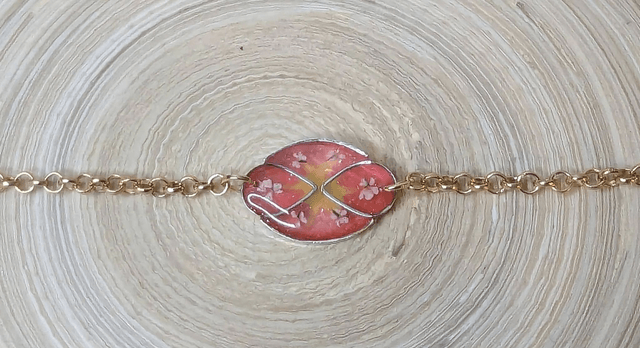 Bracelet ave une chaine de couleur or, pendentif en résine rose et jaune avec des petites fleurs blanches, le fermoir est or.