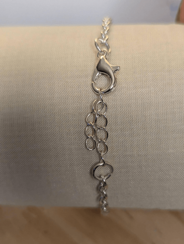  Bracelet avec une chaine de couleur argent, un pendentif en résine noir avec des fleurs séchés, le fermoir est en argent.