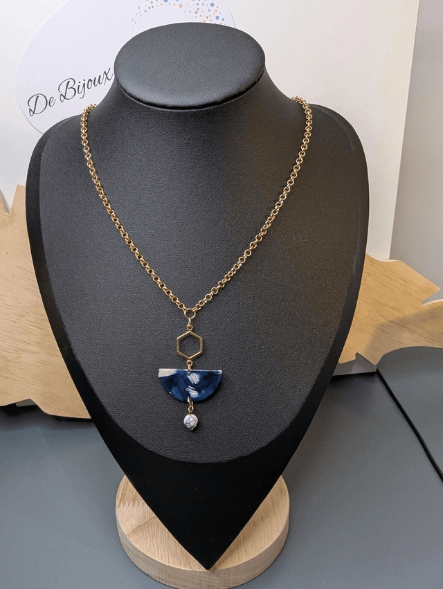 Collier mi long avec une chaine de couleur or et un pendentif en résine bleu et blanc, et un pendentif en métal doré. 
