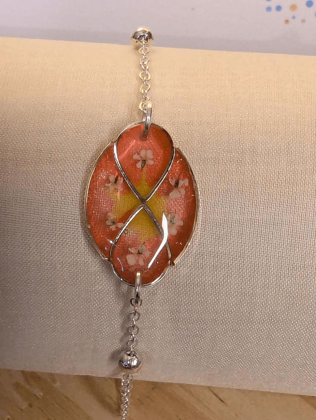Bracelet avec une chaine de couleur argent, un pendentif résine rose et jaune avec fleurs, le fermoir est en argent. 