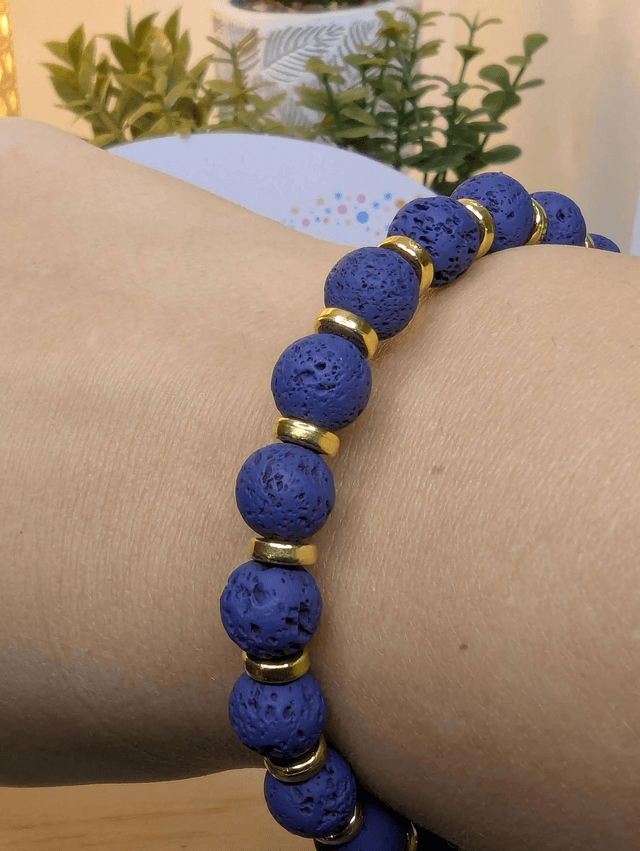 Bracelet en pierre de lave bleu foncé, avec des perles d'espacement doré. Le fermoir et la chaine fermoir sont de couleur or.