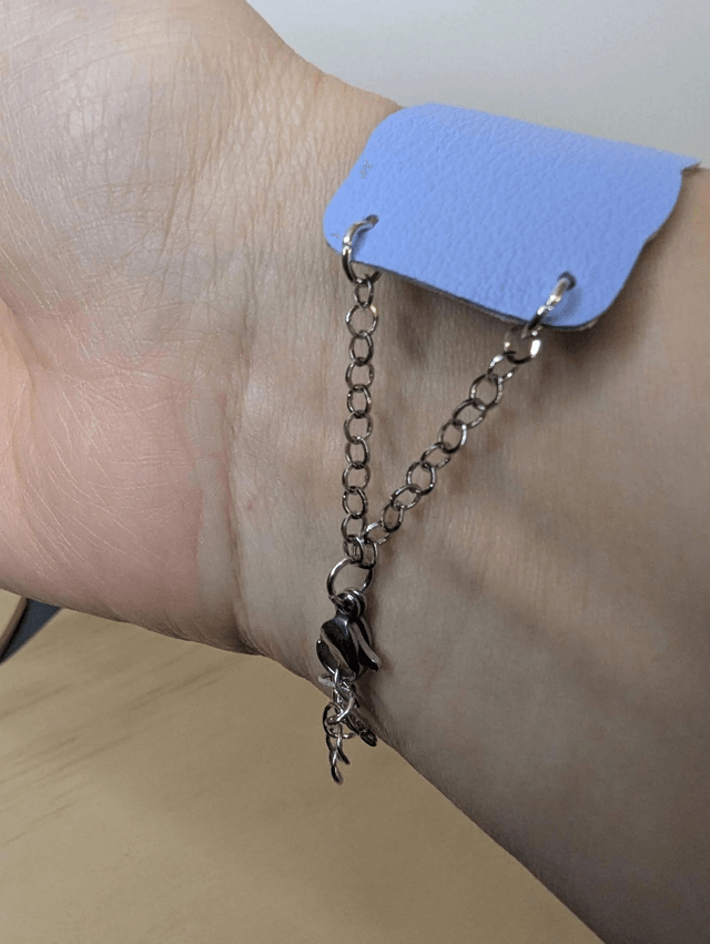 Bracelet manchette en cuir bleu lisse, avec du tissus enduit blanc (résistant), une chaine couleur argent. Le fermoir est de couleur argent.