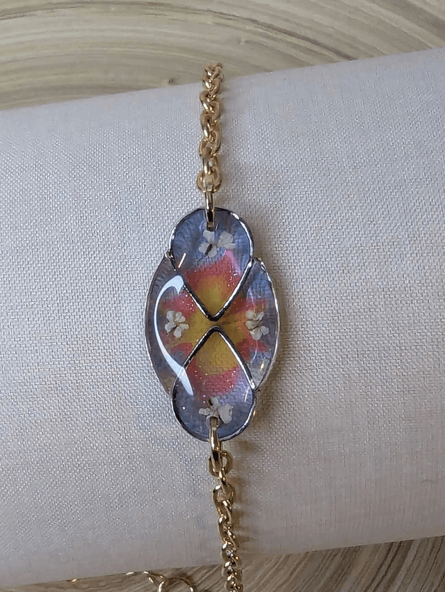 Bracelet avec une chaine de couleur or, pendentif en résine bleu, rose et jaune avec des petites fleurs blanches, le fermoir est en or.