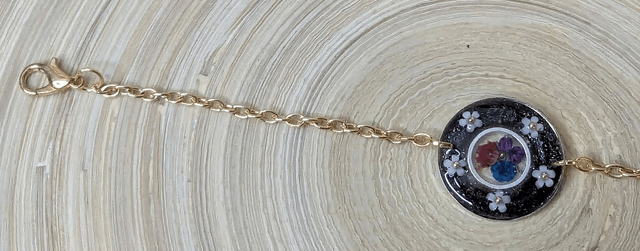 Bracelet avec une chaine de couleur or, le pendentif est en résine noir avec des fleurs séchés, le fermoir est en or. 
