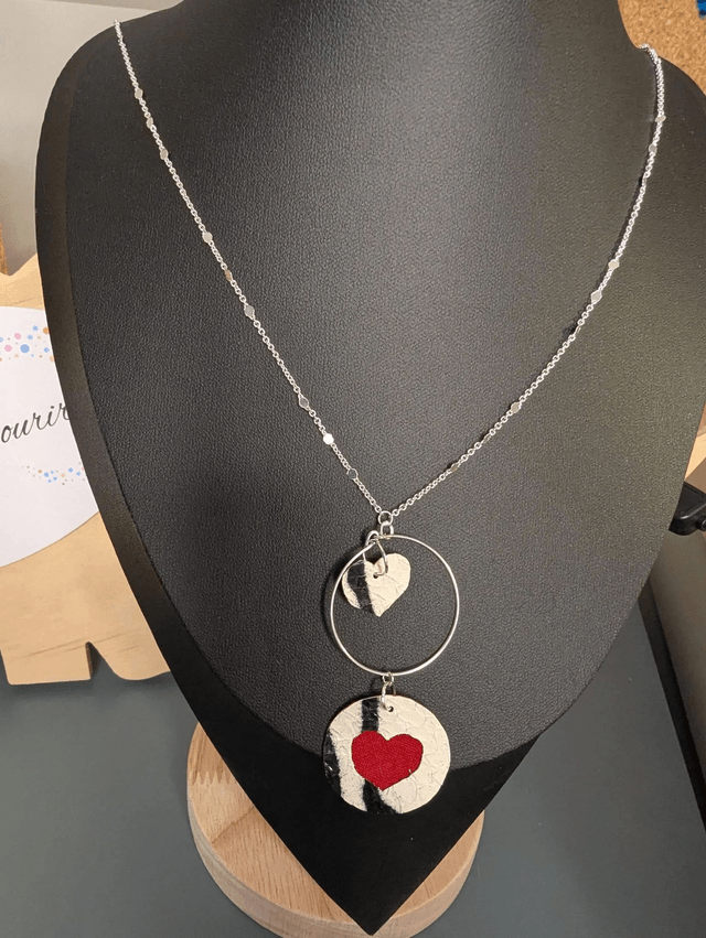 Collier long, sautoir, avec une chaine de couleur argent, un pendentif en cuir et en tissus enduit en forme de rond et de cœur
