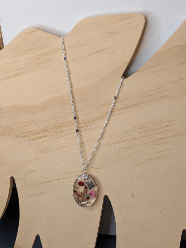 Collier mi long avec une chaine de couleur argent et un pendentif en résine avec des fleurs séchés rouge et rose. 