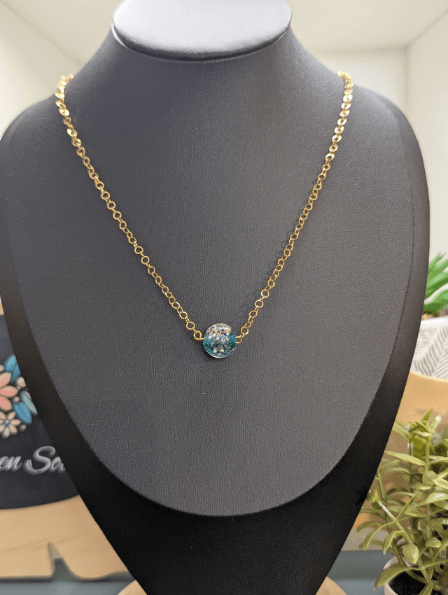 collier mi long avec chaine de couleur or et pendentif en verre de couleur bleu foncé.