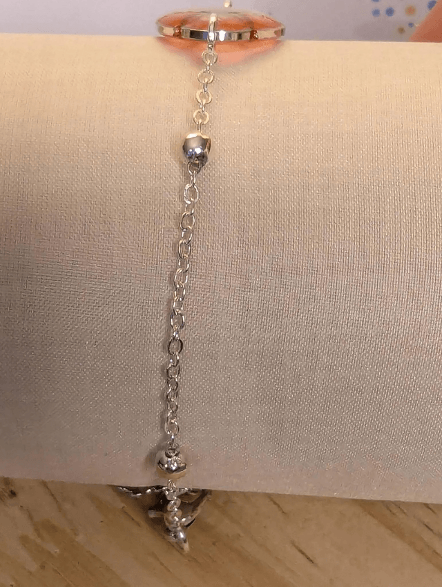 Bracelet avec une chaine de couleur argent, un pendentif résine rose et jaune avec fleurs, le fermoir est en argent. 