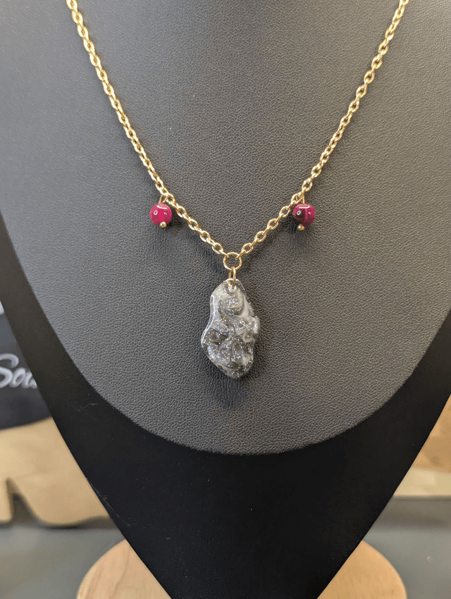 Collier mi long avec une chaine de couleur argent, un pendentif en résine noire et gris pailleté et des perles naturelles rose. 